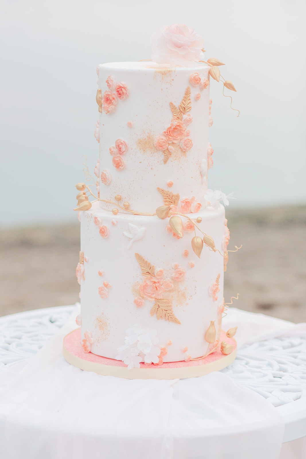 Stunning two tiered white wedding cake with gold and pink floral details