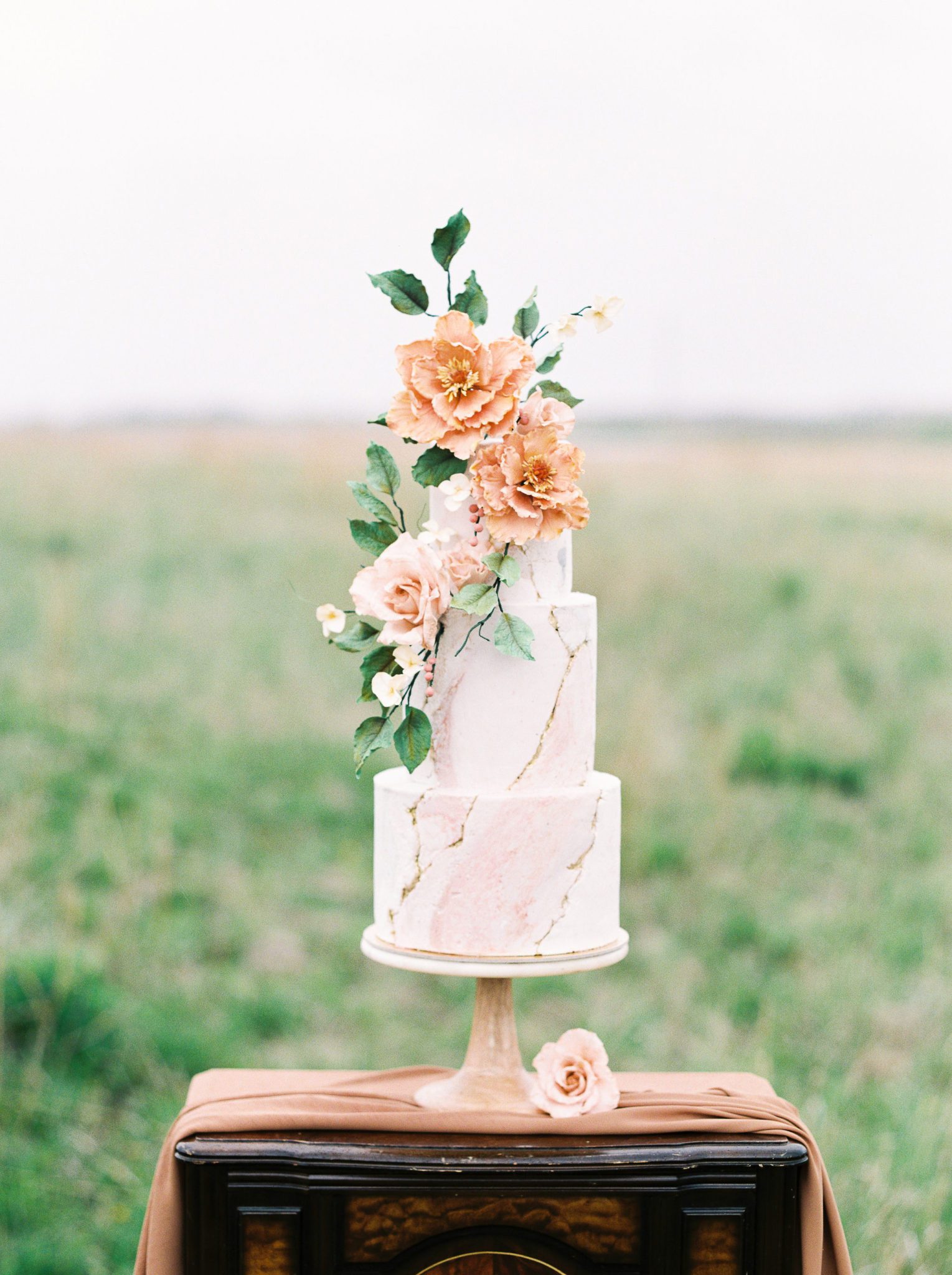 Towering marbled wedding cake with gold details and peach flowers