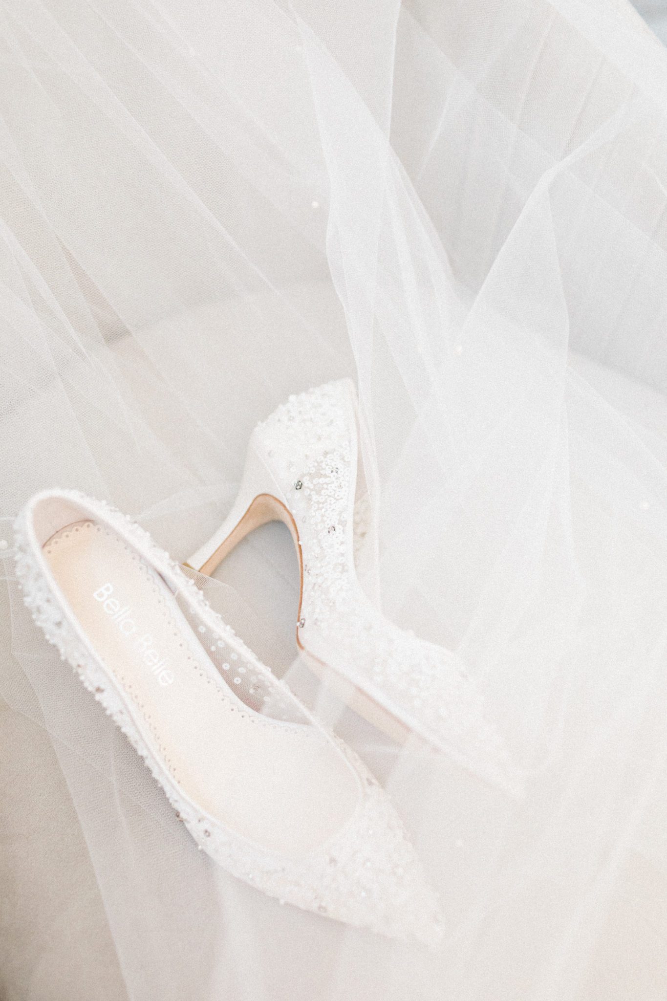 White bridal high heels photographed with bridal veil