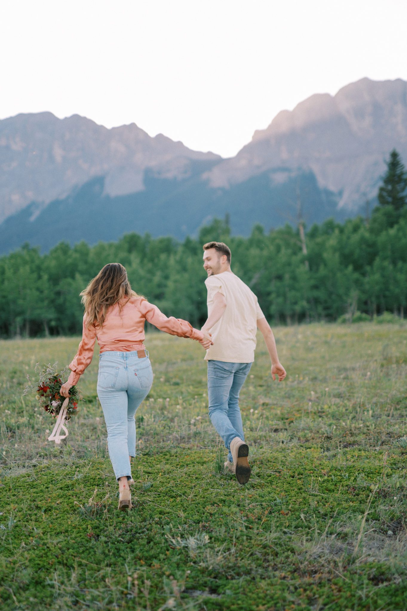 Couple frolicking in the mountains with a vibrant bouquet of flowers