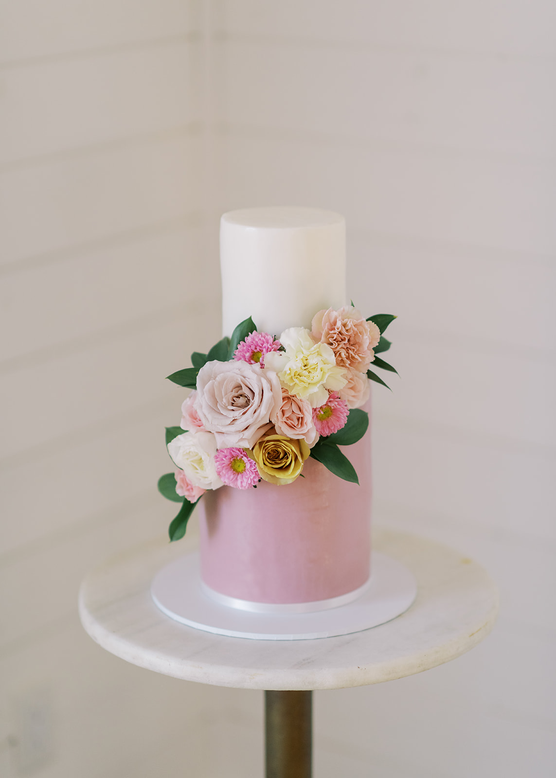 Two-tiered pink and white wedding cake with matching florals