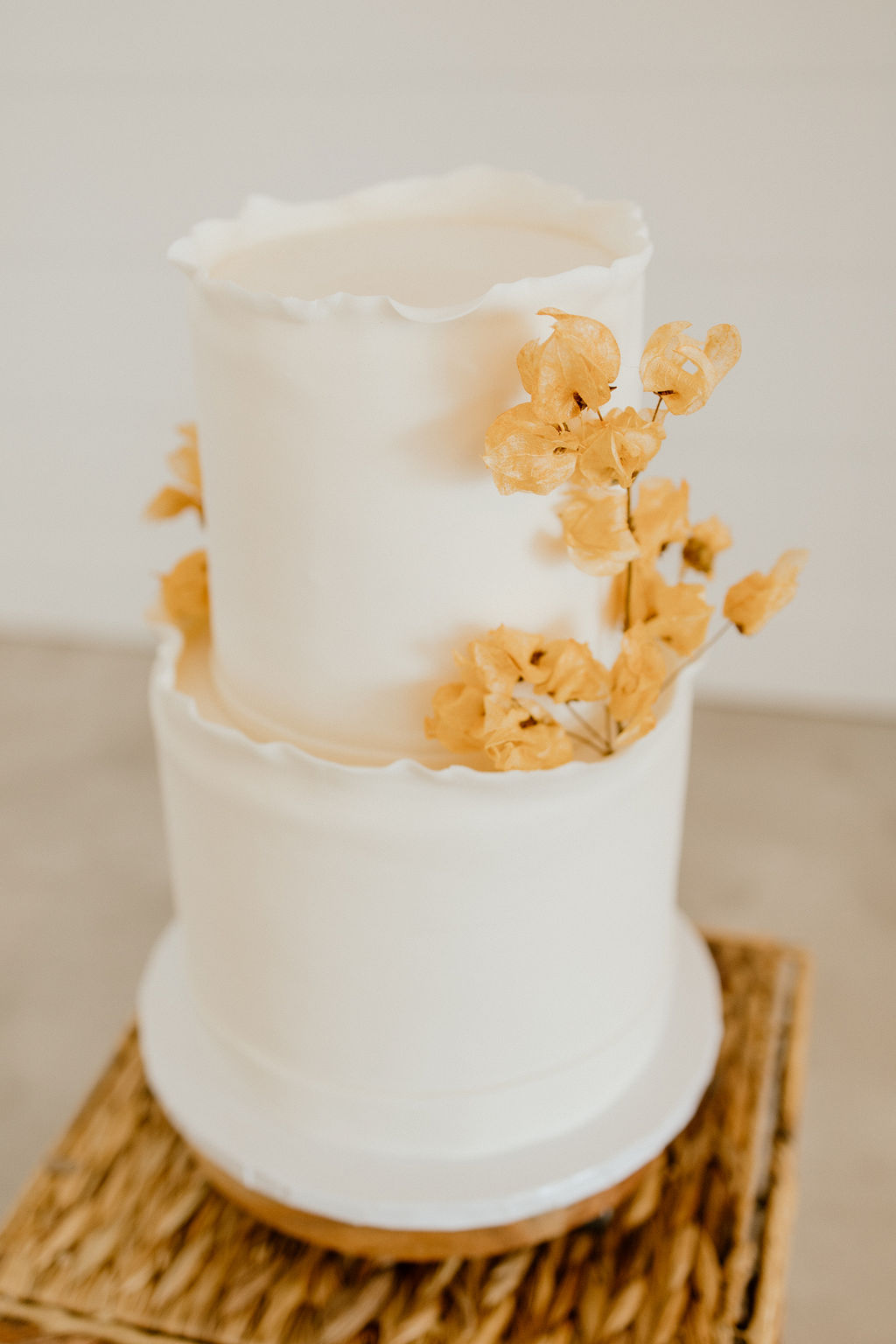 Two tiered ruffled white wedding cake with dried florals