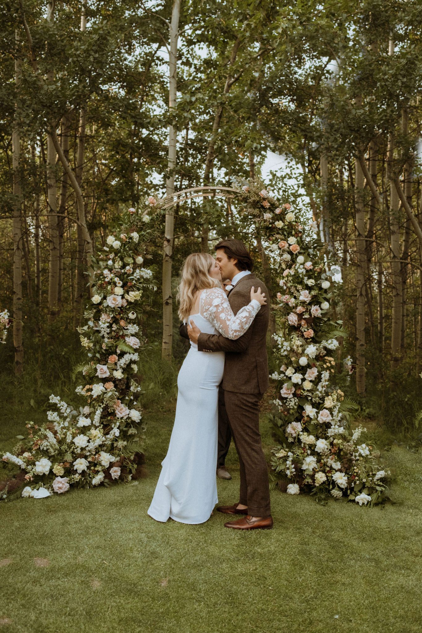 Bride and groom pose under dusty pink and green floral arch at summer wedding