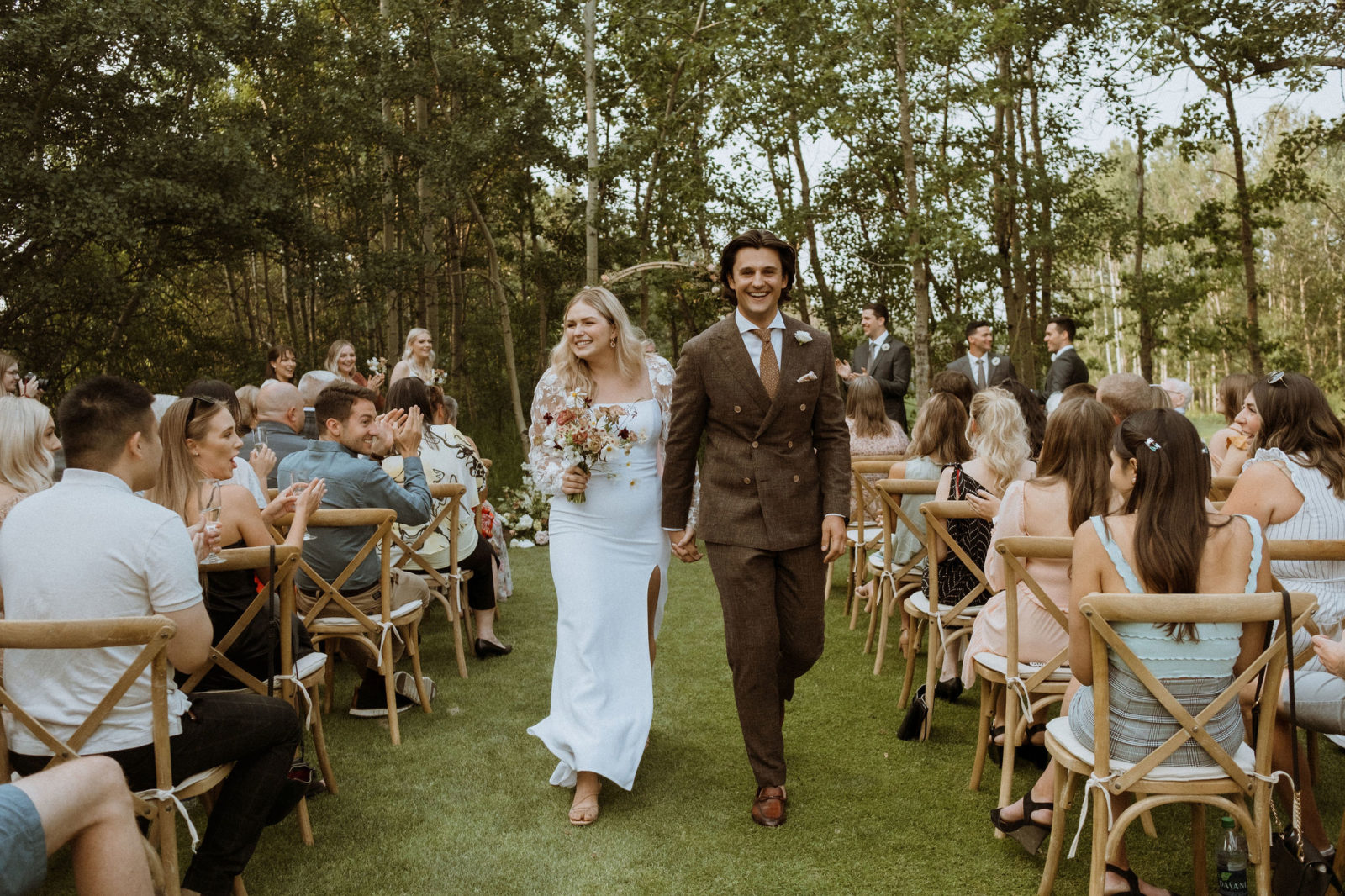 Mr and Mrs walk the aisle at this outdoor summer surprise wedding featuring a dramatic floral arch