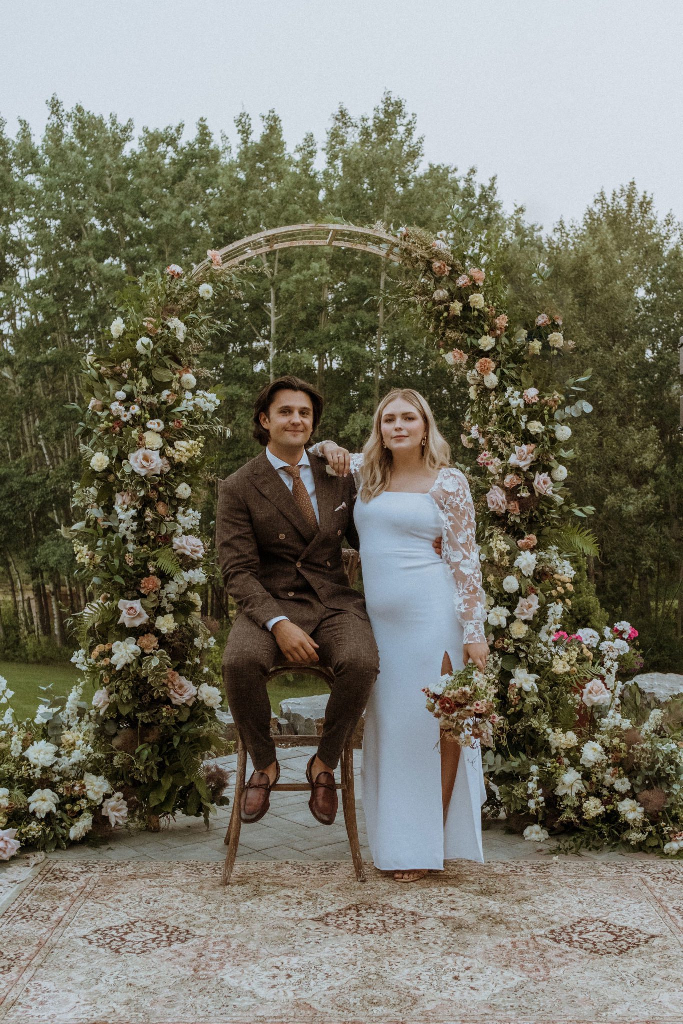 Couple pose for wedding portraits under floral arch, cottage core aesthetic, unique wedding wear