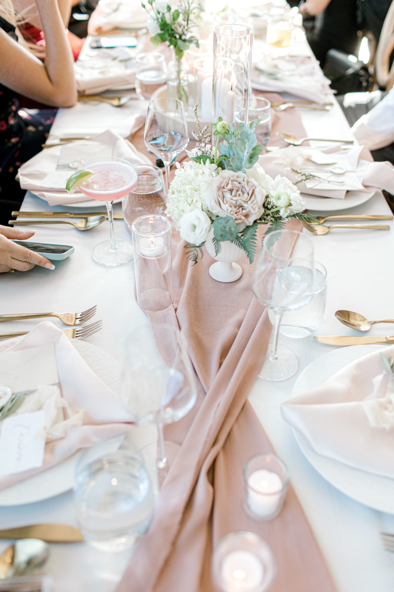Wedding table photo above showcasing place settings, gold cutlery, blush linens, white and green florals and greenery, altogether a classic yet modern wedding table design at The Sensory in Canmore Alberta