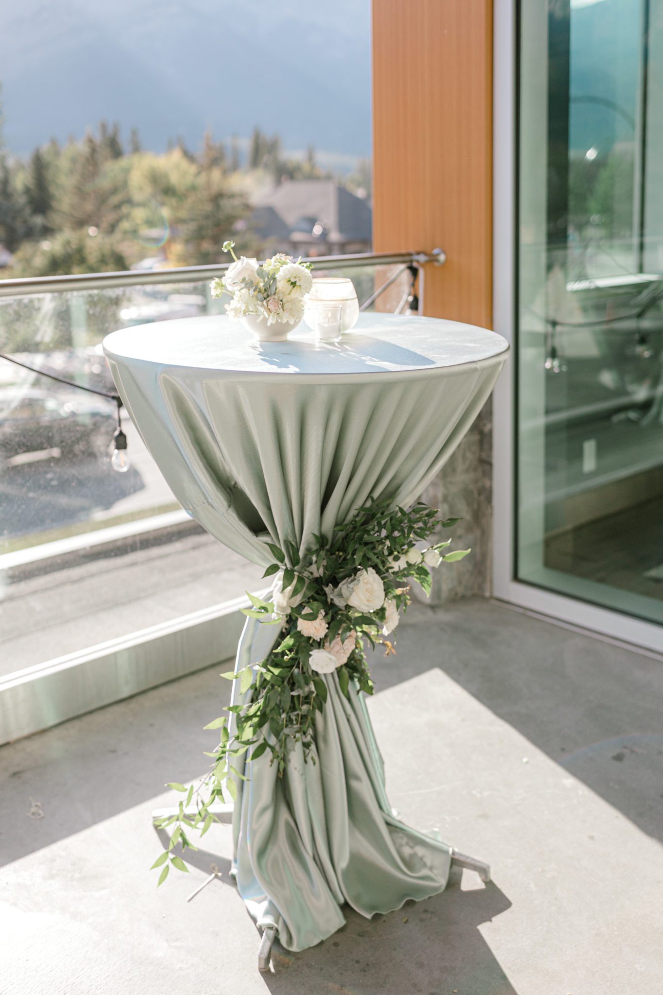 Cocktail table with sage satin linen and greenery at a wedding at The Sensory in Canmore