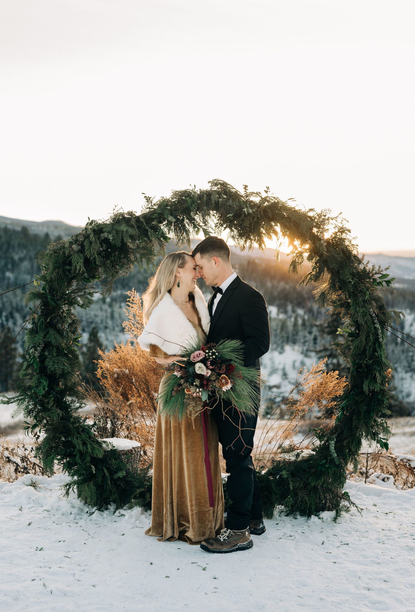 Couple celebrates outdoor elopement in the Okanagan at golden hour, custom winter archway with winter pines