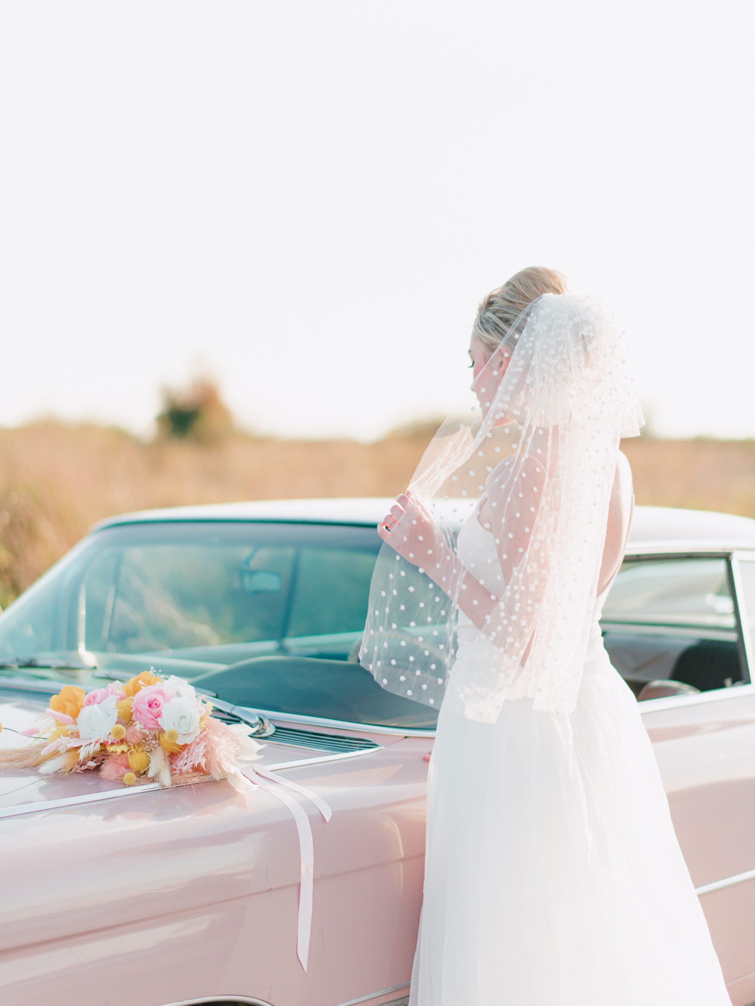 Retro bridal style featuring polka dot veil and pink and yellow bouquet, modern bouquet inspiration with pink Cadillac