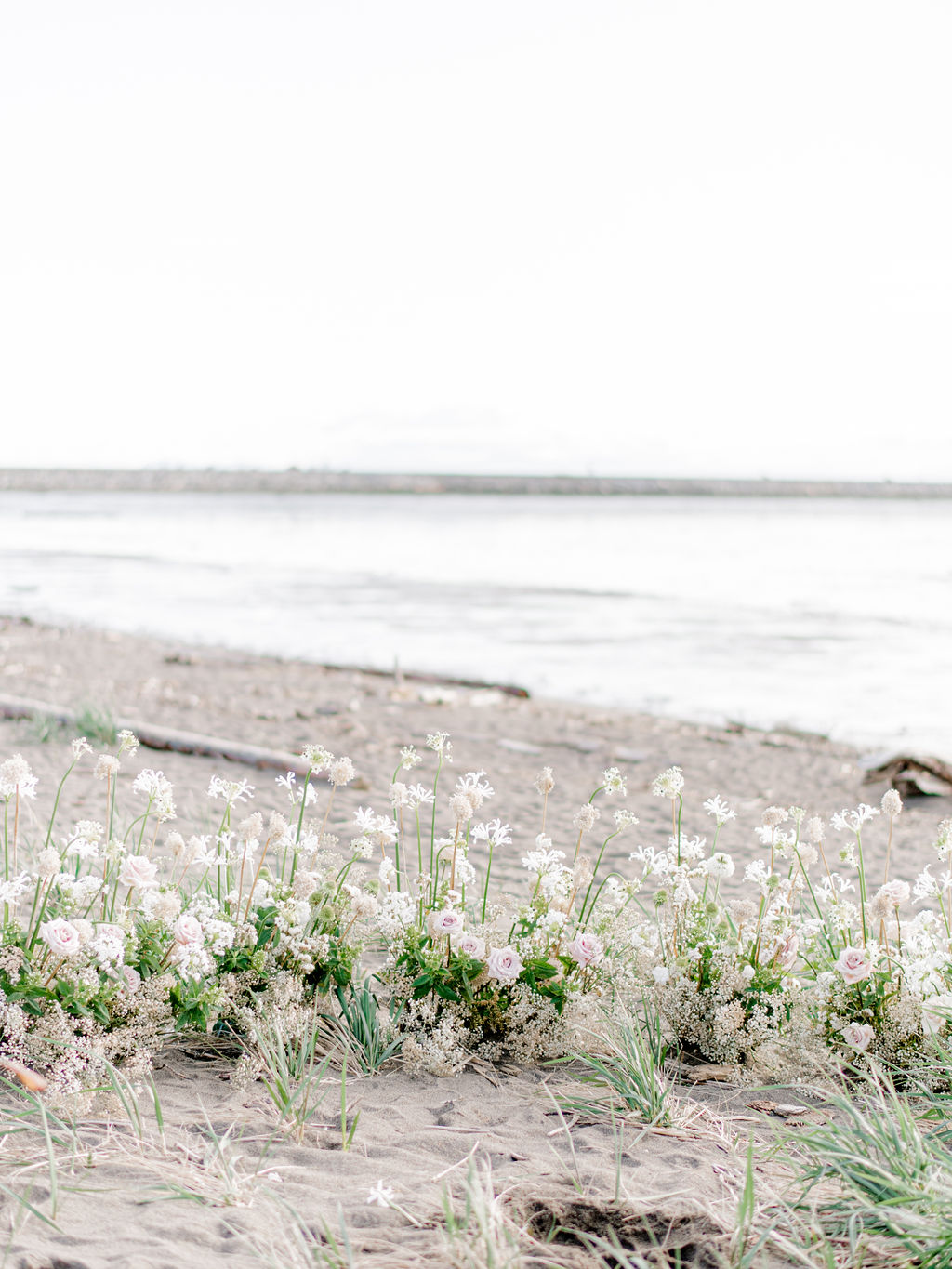 Romantic beach wedding ceremony in Vancouver, British Columbia; Fine art wedding inspiration for an intimate beach wedding, grounded floral arch with organic greenery and blush and sand coloured florals in front of the ocean