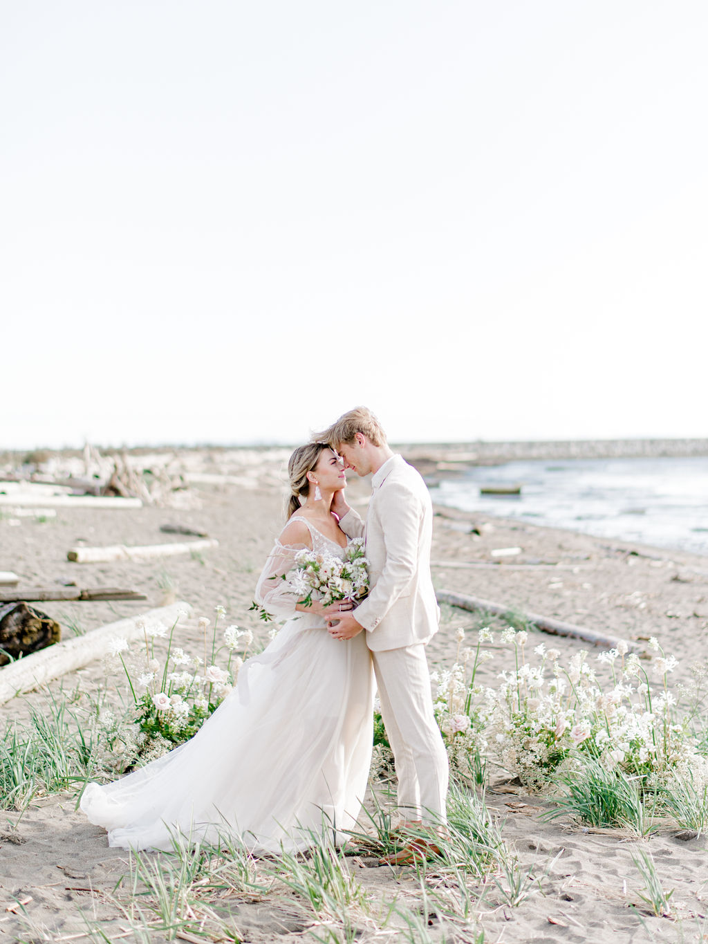 Romantic beach wedding ceremony in Vancouver, British Columbia; Fine art wedding inspiration for an intimate beach wedding, romantic wedding portraits in front of a grounded floral arch with organic greenery and blush and sand coloured florals in front of the ocean