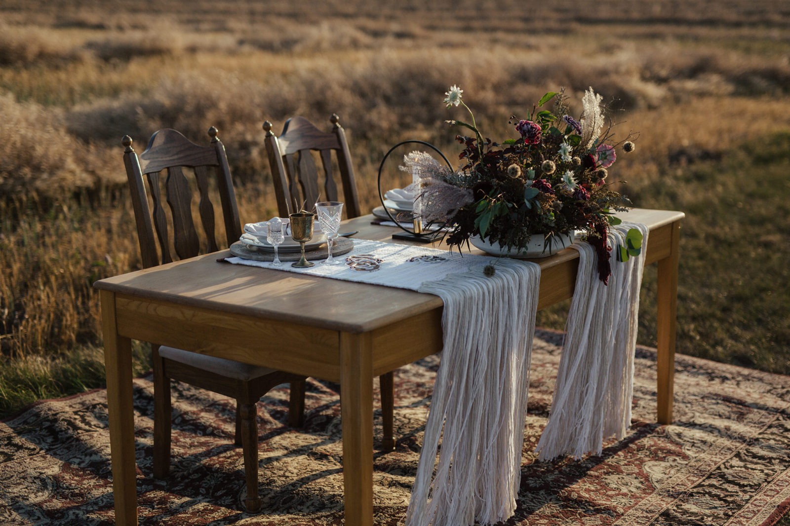 Autumn-inspired tablescape with rich coloured floral arrangements, placed on top of a wooden sweetheart table for the bride and groom, with cream-coloured drapery and vintage glassware, fall vow renewal inspiration. 