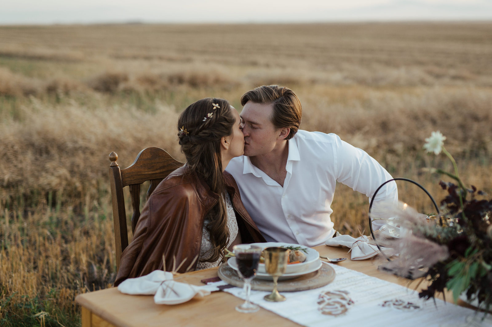 Portrait of bride and groom sharing a kiss while seated at their autumn-inspired sweetheart table, located in the rural Alberta countryside, fall vow renewal inspiration. 