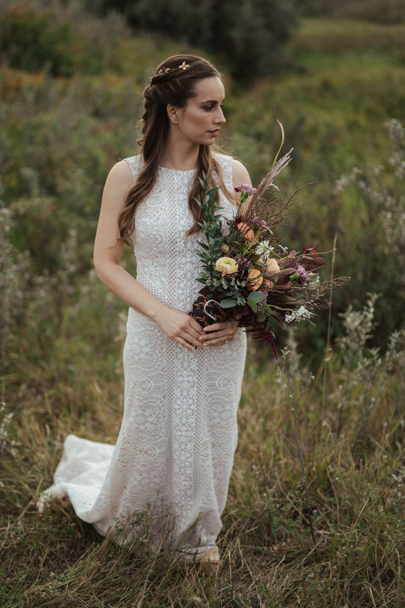 Portrait of bride in rural Alberta countryside, wearing lace-detailed gown and holding fall-coloured bouquet. 