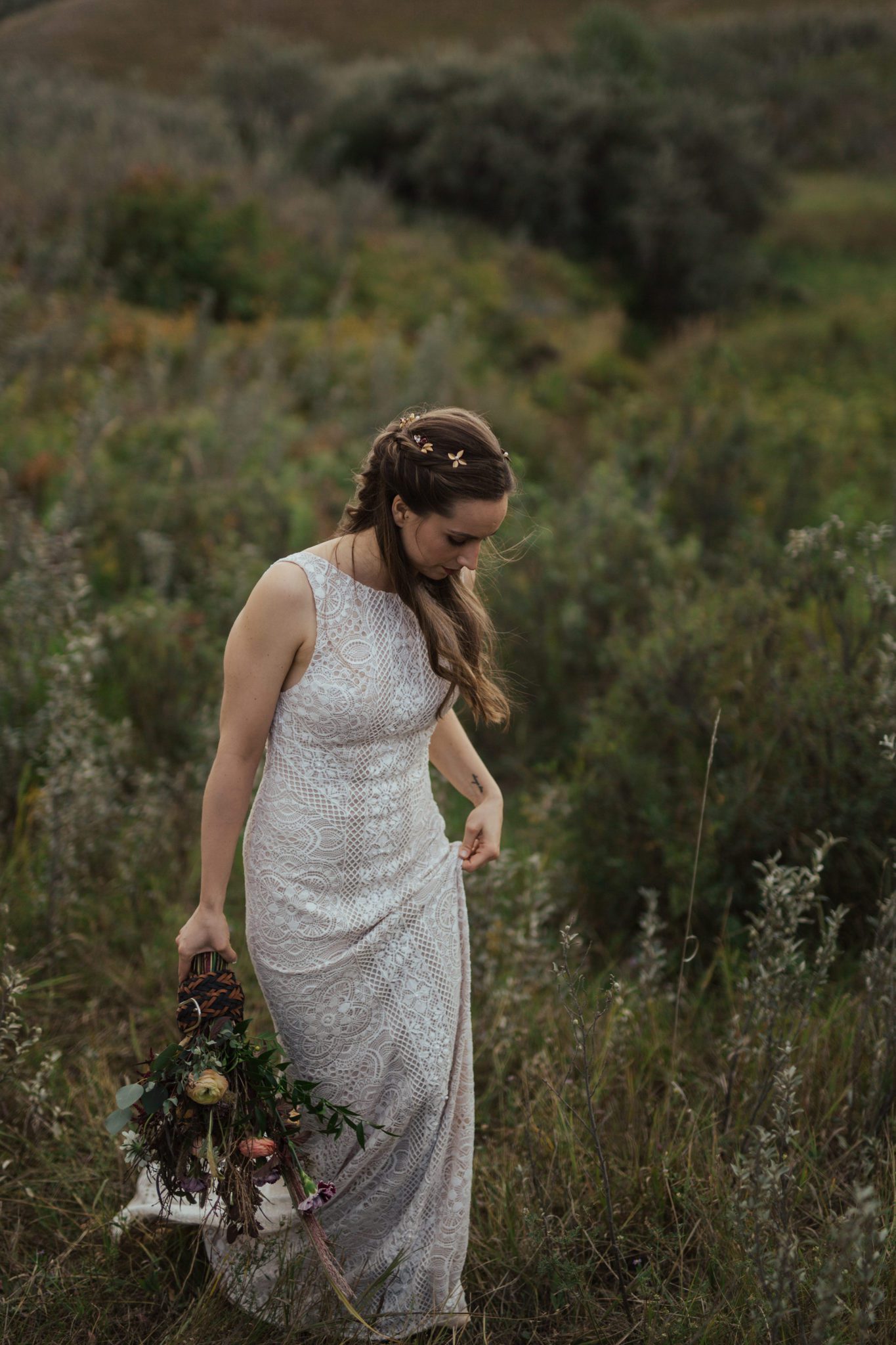Portrait of bride frolicking in rural Alberta countryside, wearing lace-detailed gown and holding fall-coloured bouquet. 