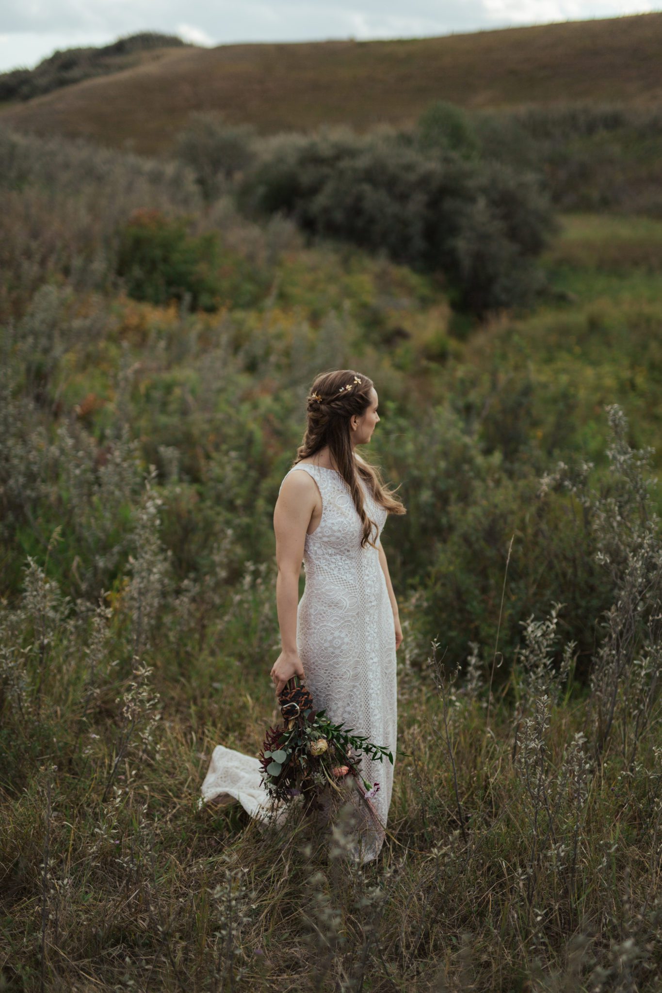 Portrait of bride in rural Alberta countryside holding fall-toned bridal bouquet, wearing lace-detailed bridal gown.
