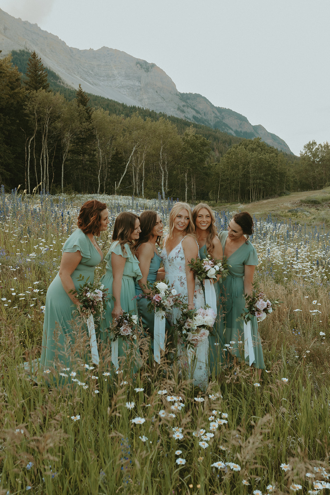 Bridal party portraits in a field of wildflowers for a mountain wedding. Sage Green mismatched bridesmaid dresses in this outdoor wedding inspiration, wildflower and mountain portraits, boho wedding inspiration, summer wedding, wedding portraits, bridal party portraits