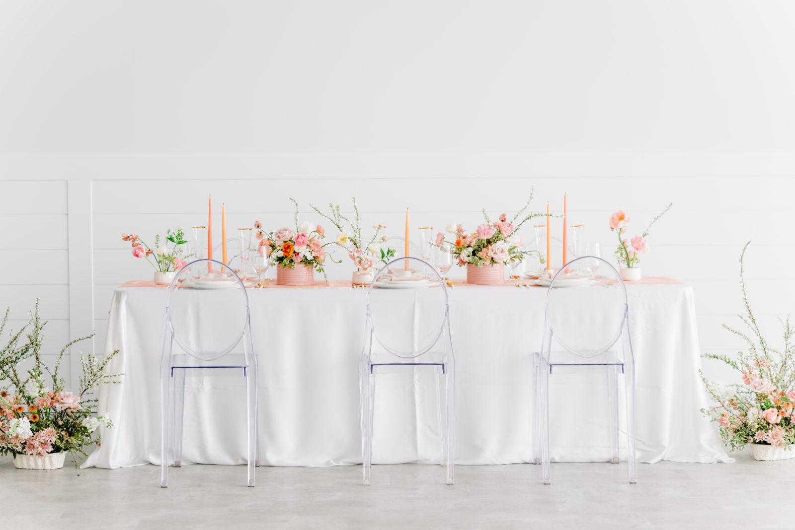 white reception table with clear seating and bright pink florals, coloured candles