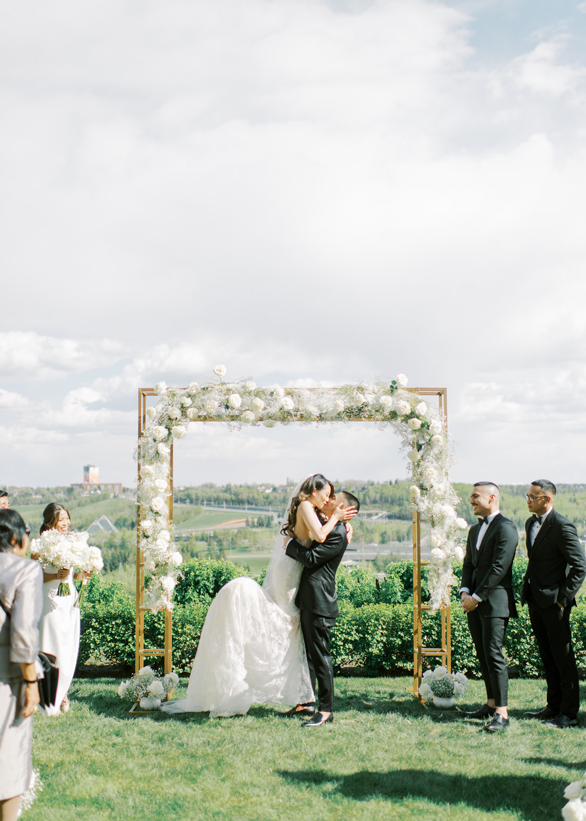 First kiss for bride and groom at outdoor wedding reception, gold and white wedding archway, black and white modern wedding