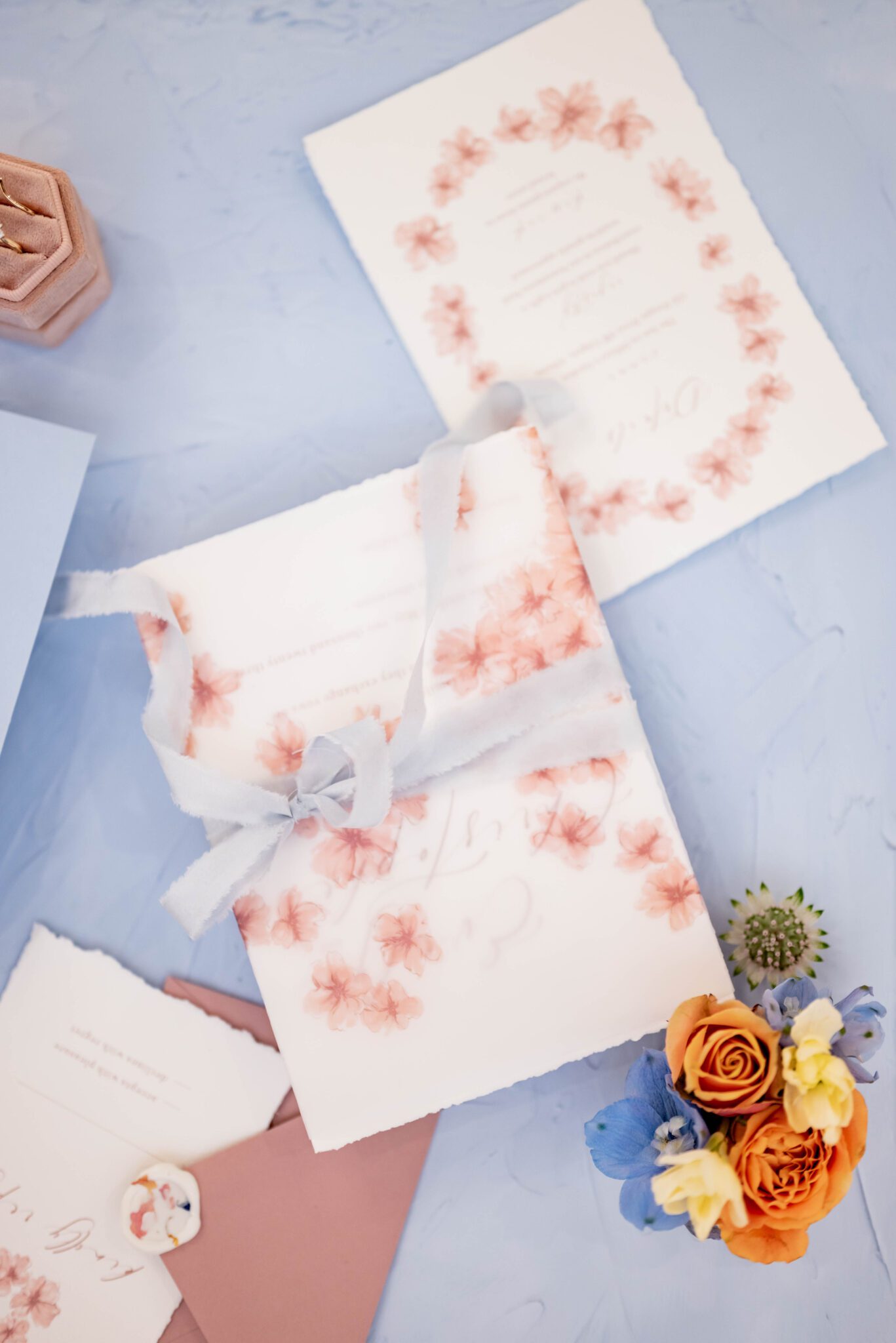 Spring inspired wedding invitation adorned with wildflower details by Seeking Light Studio, wedding stationery flat lay on baby blue velvet linen, wedding details photo inspiration featuring spring wild flowers in blue, orange and yellow