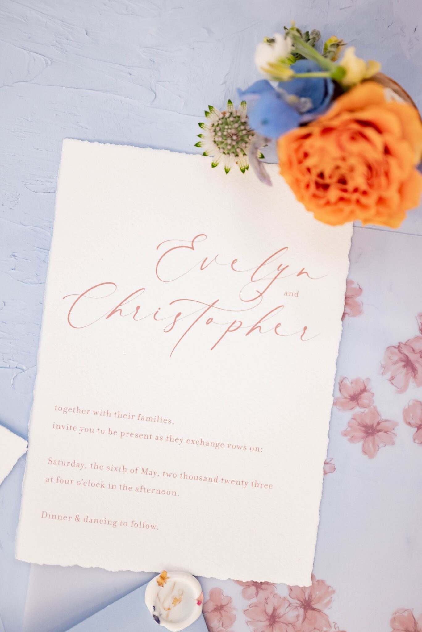 wedding invitation stationery flat lay on baby blue background, wedding details photo inspiration featuring spring wild flowers in blue, orange and green