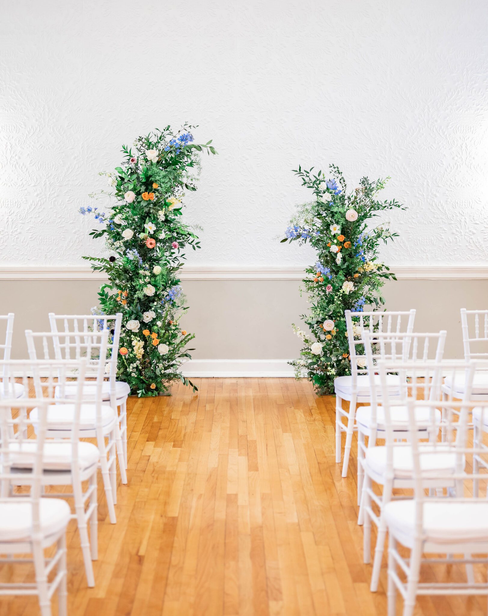 Stunning column floral arch with lush greenery as a focal point of the an indoor ceremony, whimsical and romantic pastel spring wedding inspiration, white chiavari chairs for guests during ceremony