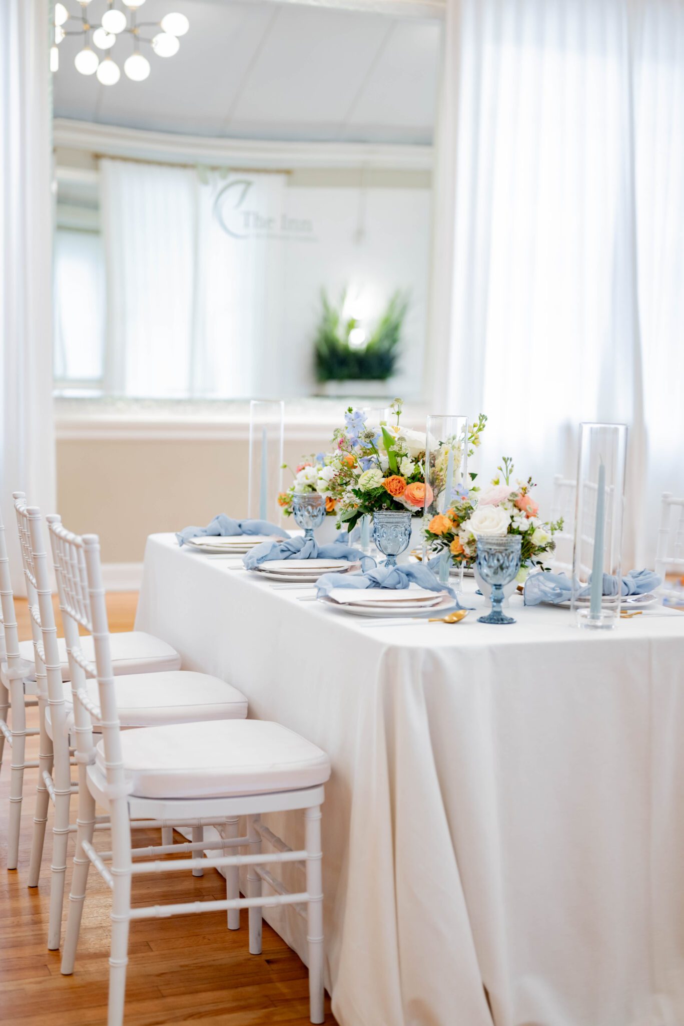 Guest tablescape featuring vintage light blue goblets and candlesticks and whimsical wildflower centrepieces, white chiavari guest chairs set up at guest table with creamy white velvet linens for spring wedding in Calgary, Alberta