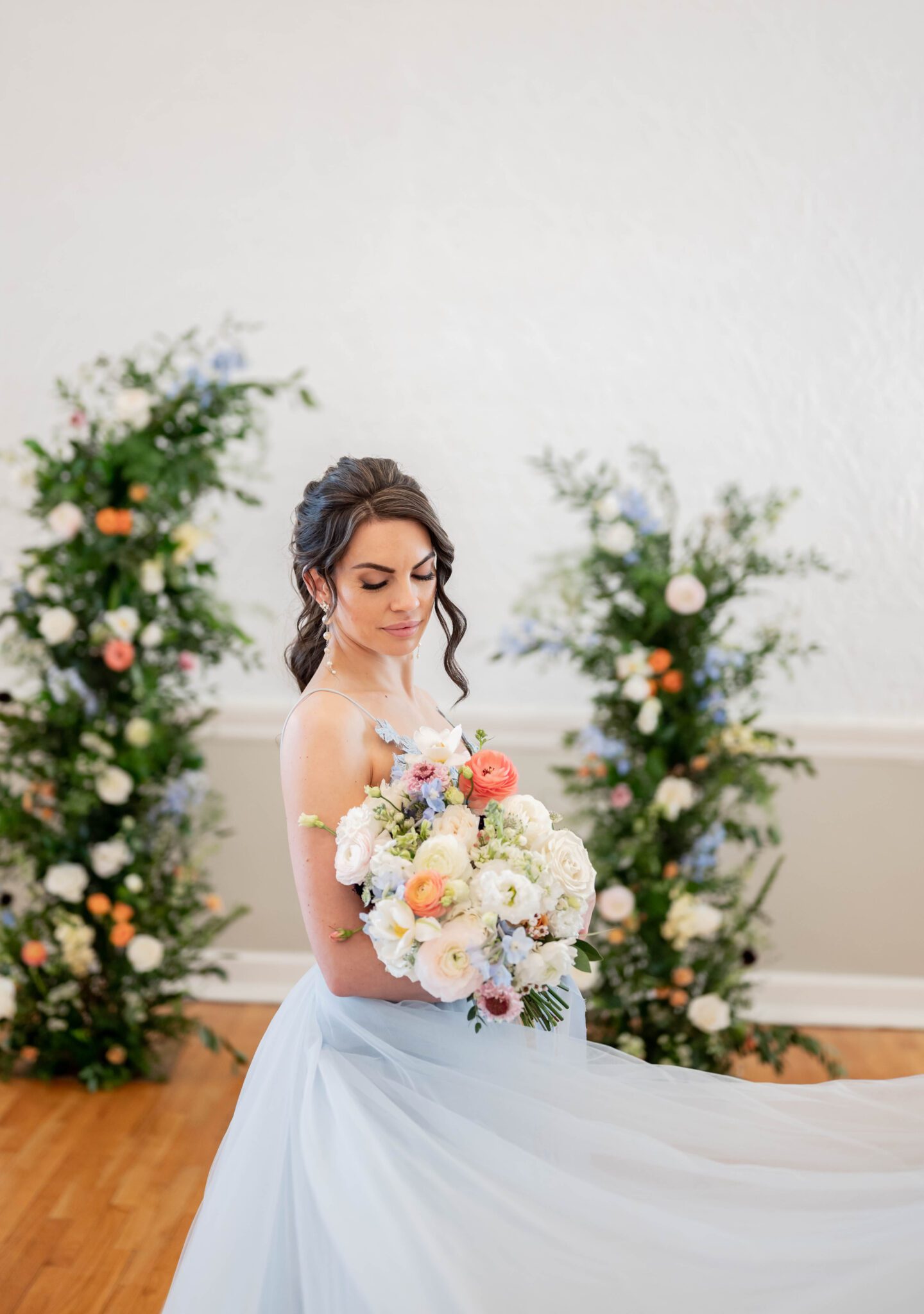 Feminine bridal portrait before ceremony holding pastel coloured bouquet, column floral arch with lush greenery as a focal point of the an indoor ceremony, baby blue wedding dress inspiration  