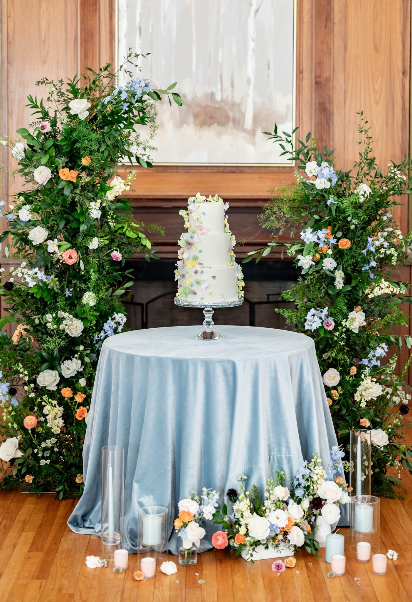 Stunning column floral arch with wildflowers and lush greenery behind dessert table, whimsical and romantic pastel wedding cake inspiration, baby blue velvet linens on dessert table