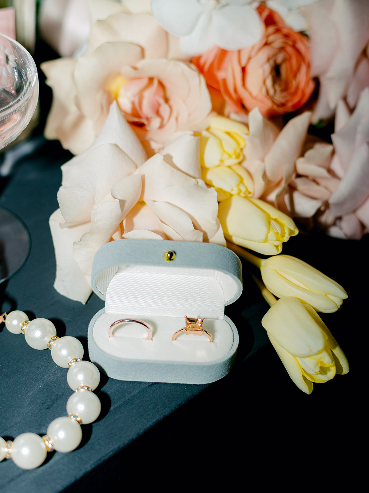 Flash photography used in flat lay photo featuring blue velvet ring box and pastel yellow and pink with a punch of bright orange in bride's bouquet