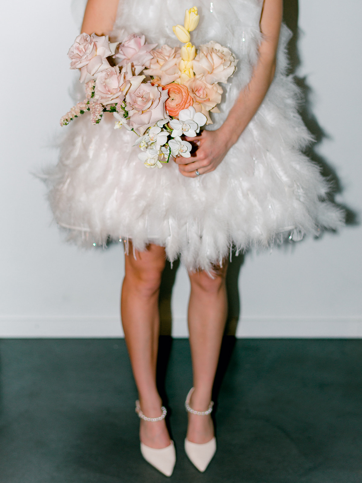 short wedding dress style, minimalistic studio venue for wedding photos highlighting the beauty of a feather bridal look, pastel yellows and pinks in bouquet with pop of orange