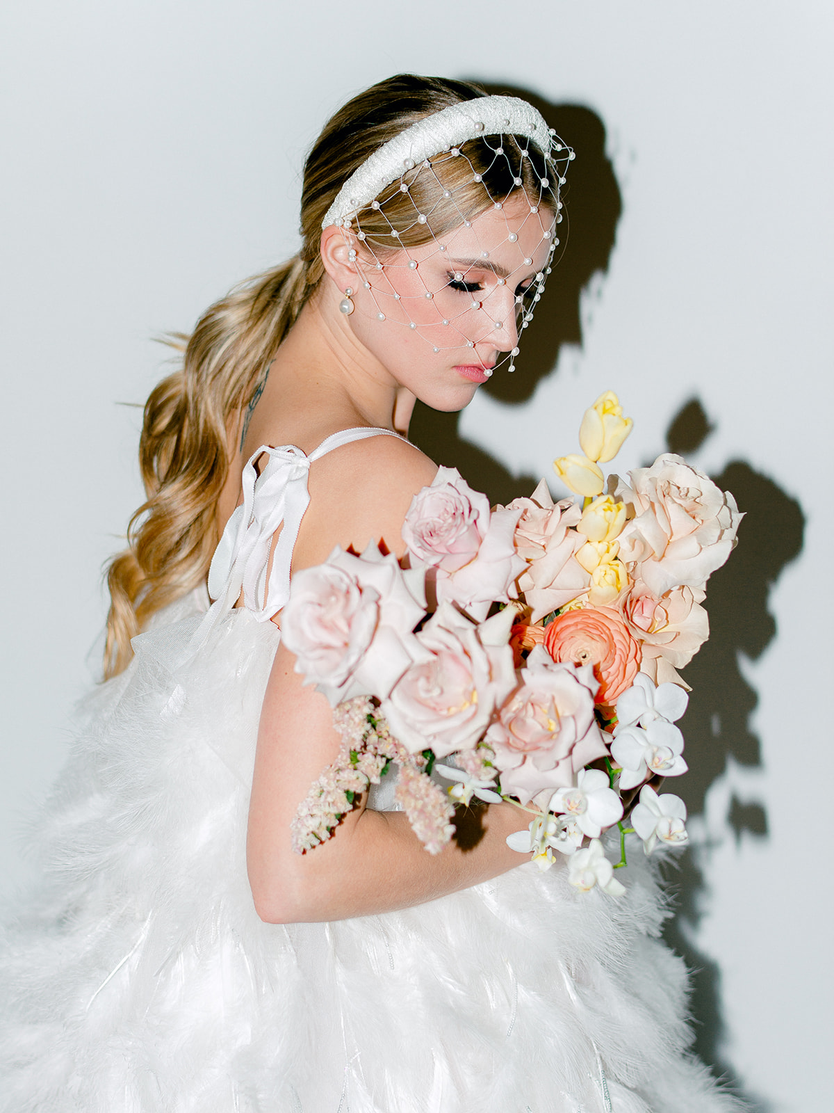 Dynamic flash photography beautifully illuminating bright florals in captivating bridal portraits, a modern and feminine aesthetic, portrait featuring a modern birdcage veil worn by a bride holding her bouquet in a feather wedding gown, low pony-tail bridal hairstyle