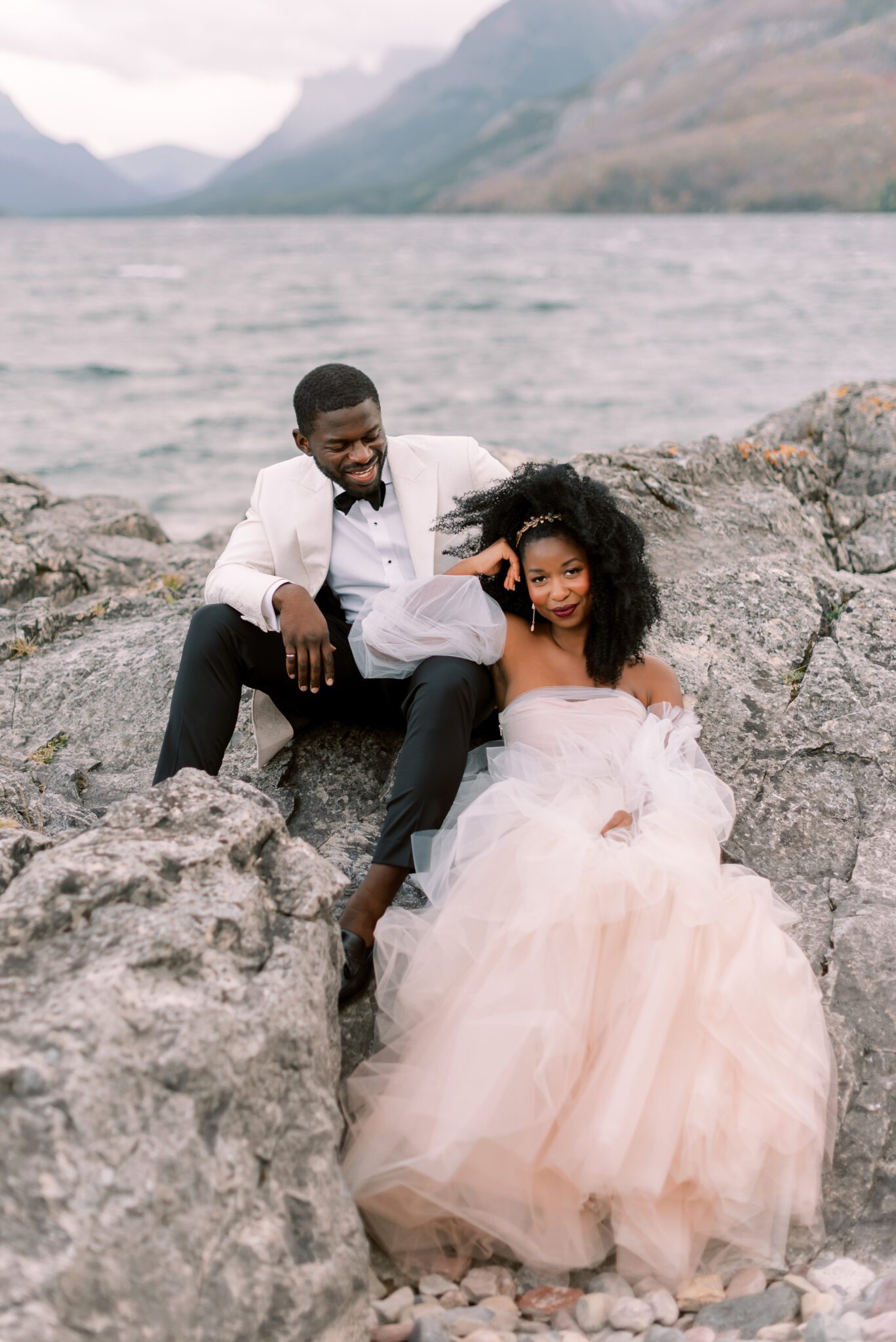 bride and groom sitting for outdoor portraits, lakeside and mountain elopement inspiration, bride wearing blush wedding dress by Alexandra Victoria Rose