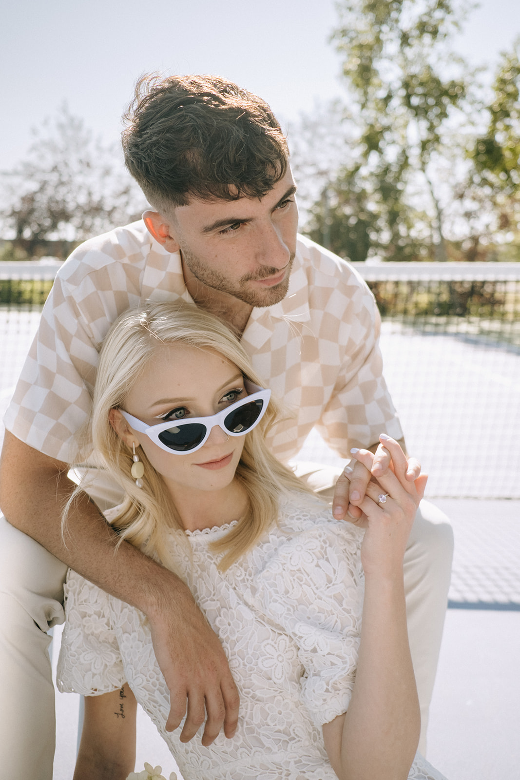 Bride is wearing white cat-eye sunglasses for bridal portrait, casual groom attire suggestions for a laid-back and comfortable vibe, sporty idea for couples portraits on a tennis court