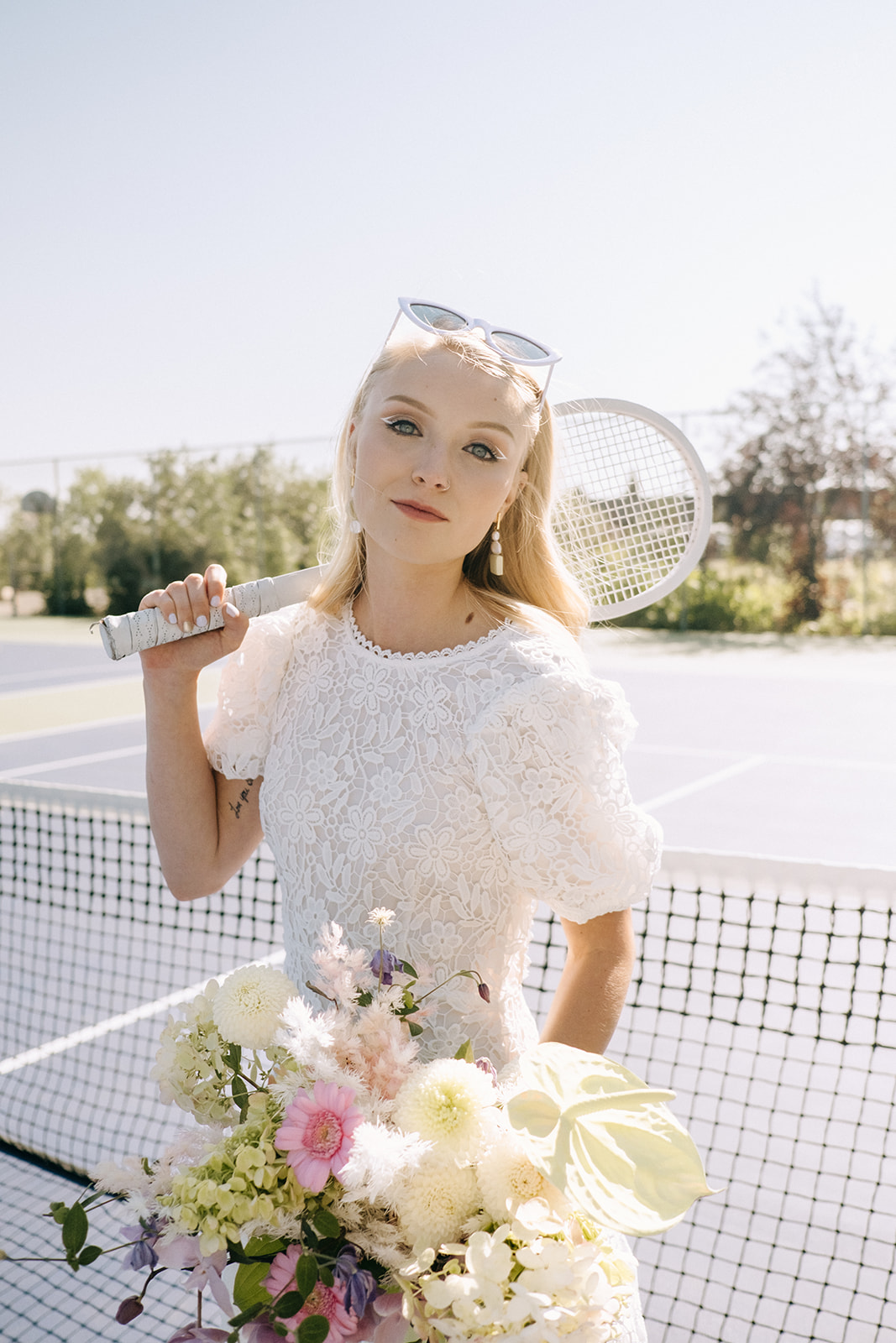 Tennis themed wedding ideas for a sporty bridal inspiration, sporty bridal make-up with white eyeliner by Madi Leigh Artistry, unique bridal portrait on a tennis court with bride holding a racquet 