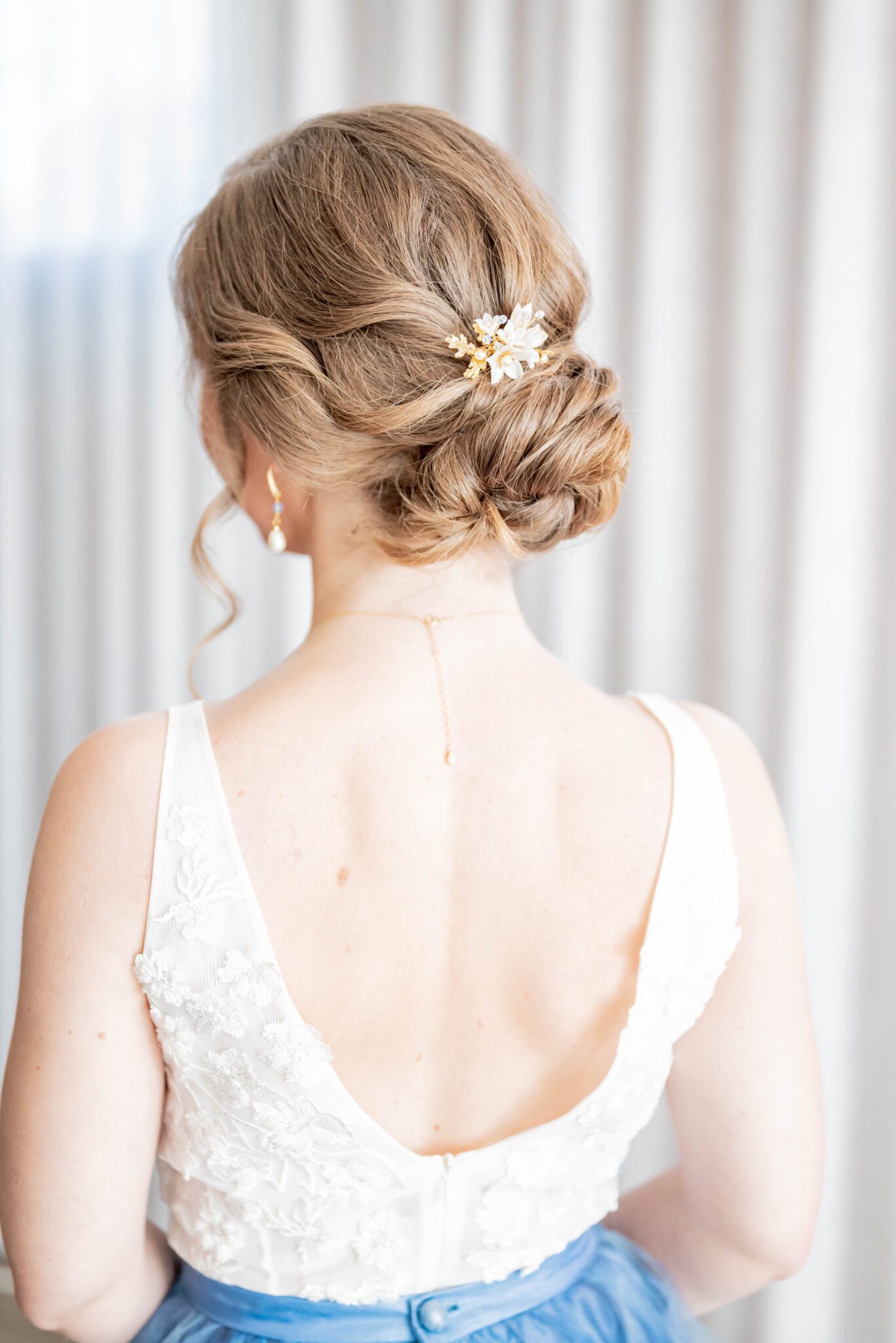 Romantic and timeless bridal up-do hairstyle with white, blue and gold floral hair pin, bridal portrait of the bride's back showcasing the low-back white lace top of her wedding dress