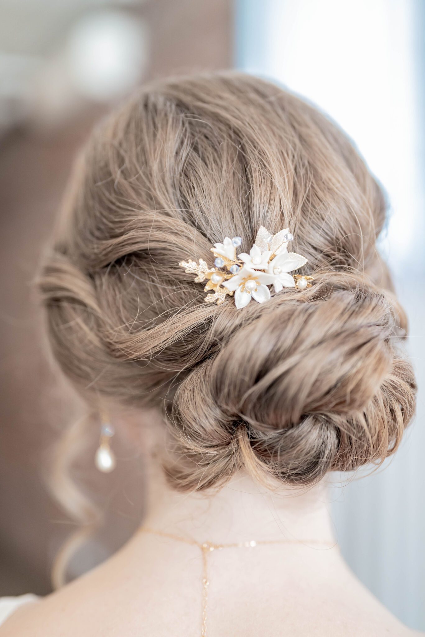 gold hair pin featuring white flowers, gold leaves and small baby blue accents in bridal up-do, romantic low-bun hairstyle for bride