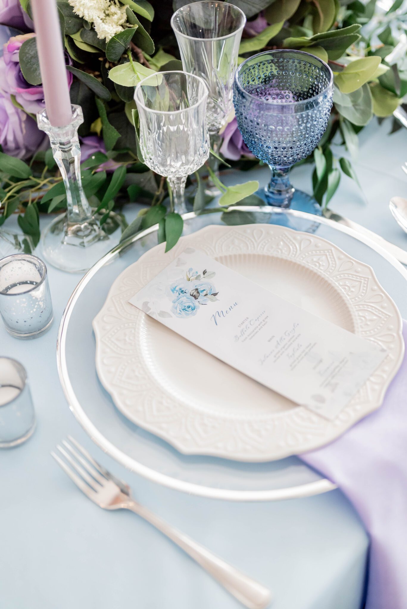 Custom menu stationery with blue florals, grey-toned vines and calligraphy, baby blue linen, pastel purple napkins, blue crystal goblets and silver mercury votives decorate reception table, lush green, purple and baby blue centrepiece ideas
