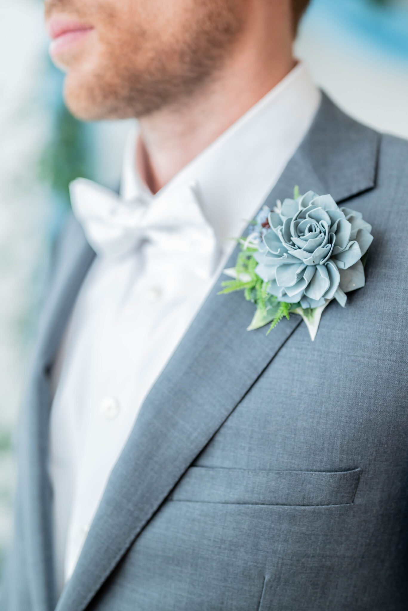 Classic grey suit with silver blue bow tie and baby blue floral boutonniere in groom portrait, grey groom attire inspiration by Thomas Jeffery Menswear