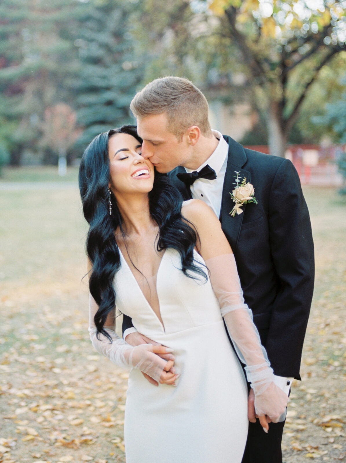 Heartwarming couples portraits in a park setting during the fall season, bridal gown with bridal gloves by Kelly Parker Atelier, modern bride hairstyle with loose curls and trendy middle part styled by Hair Designs by Maggie