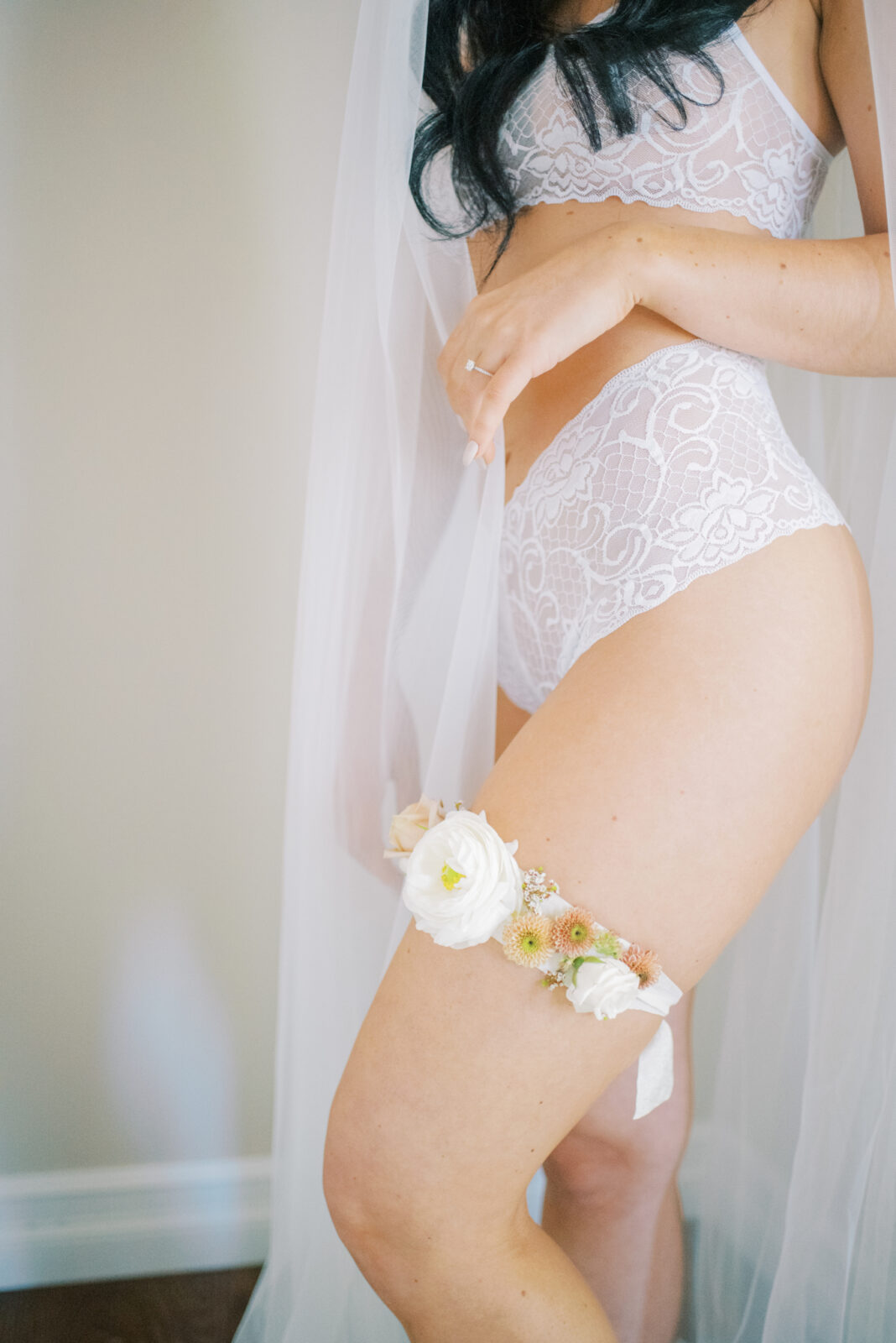 romantic bridal boudoir portraits with floral garter in a fall theme colour palette, white lace wedding day lingerie inspiration, bride wearing a long veil showing floral garter in intimate photoshoot