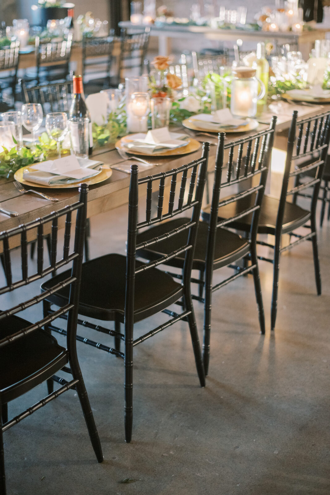 black chiavari chairs for guests during wedding modern wedding reception, fall wedding florals with lush greenery on guest tables, gold charger place settings on long wood tables