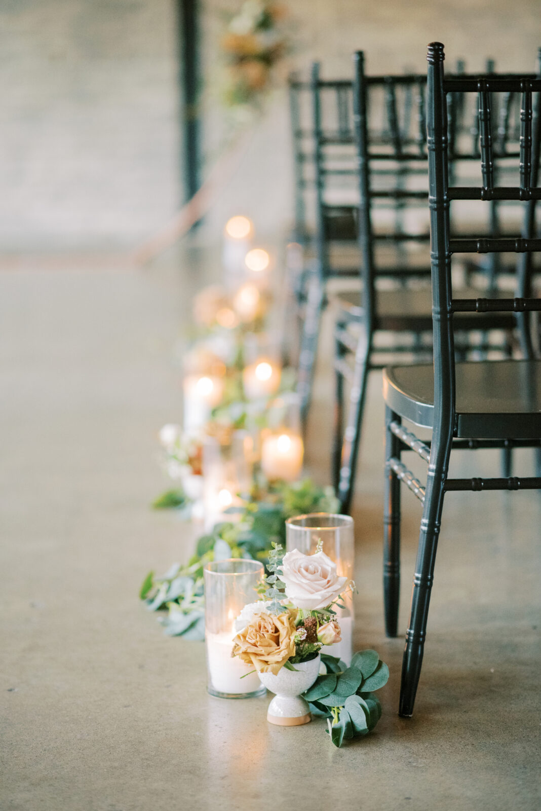 black chiavari guest chairs for modern and classic ceremony style, indoor wedding ceremony with candles, florals and greenery lining the aisle, industrial wedding venue with concrete floor in Edmonton, Alberta