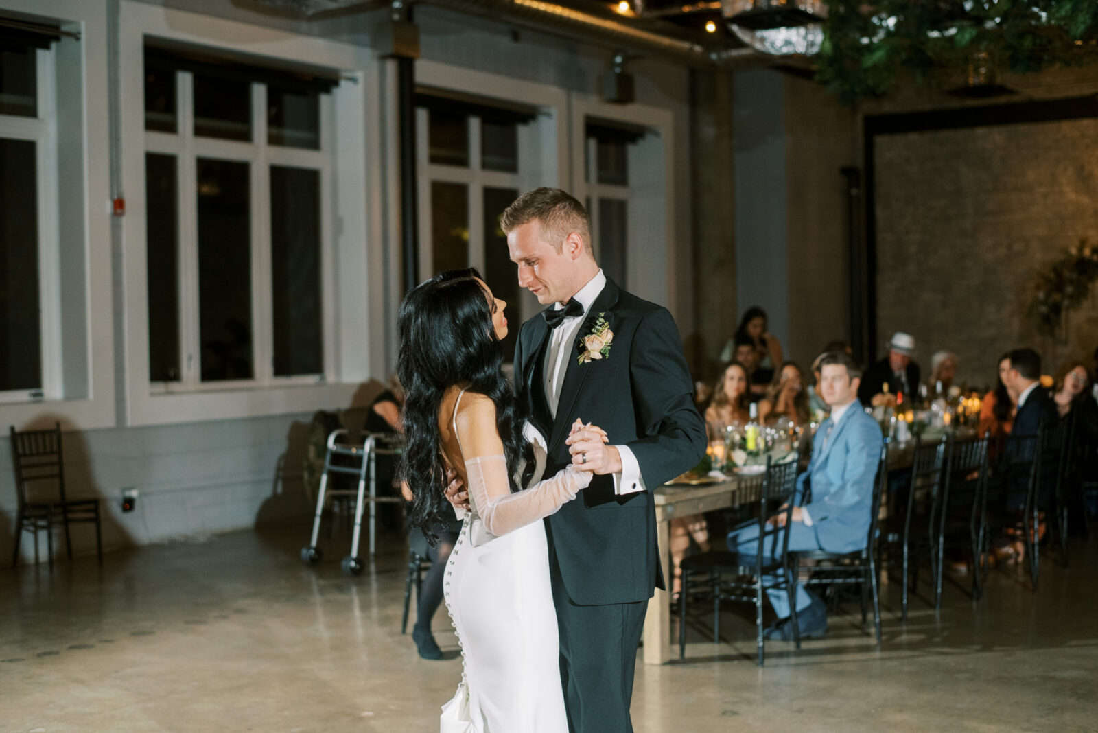 Bride and groom first dance, chic and modern bridal gown featuring sheer sleeves, industrial wedding reception venue in Edmonton, Alberta