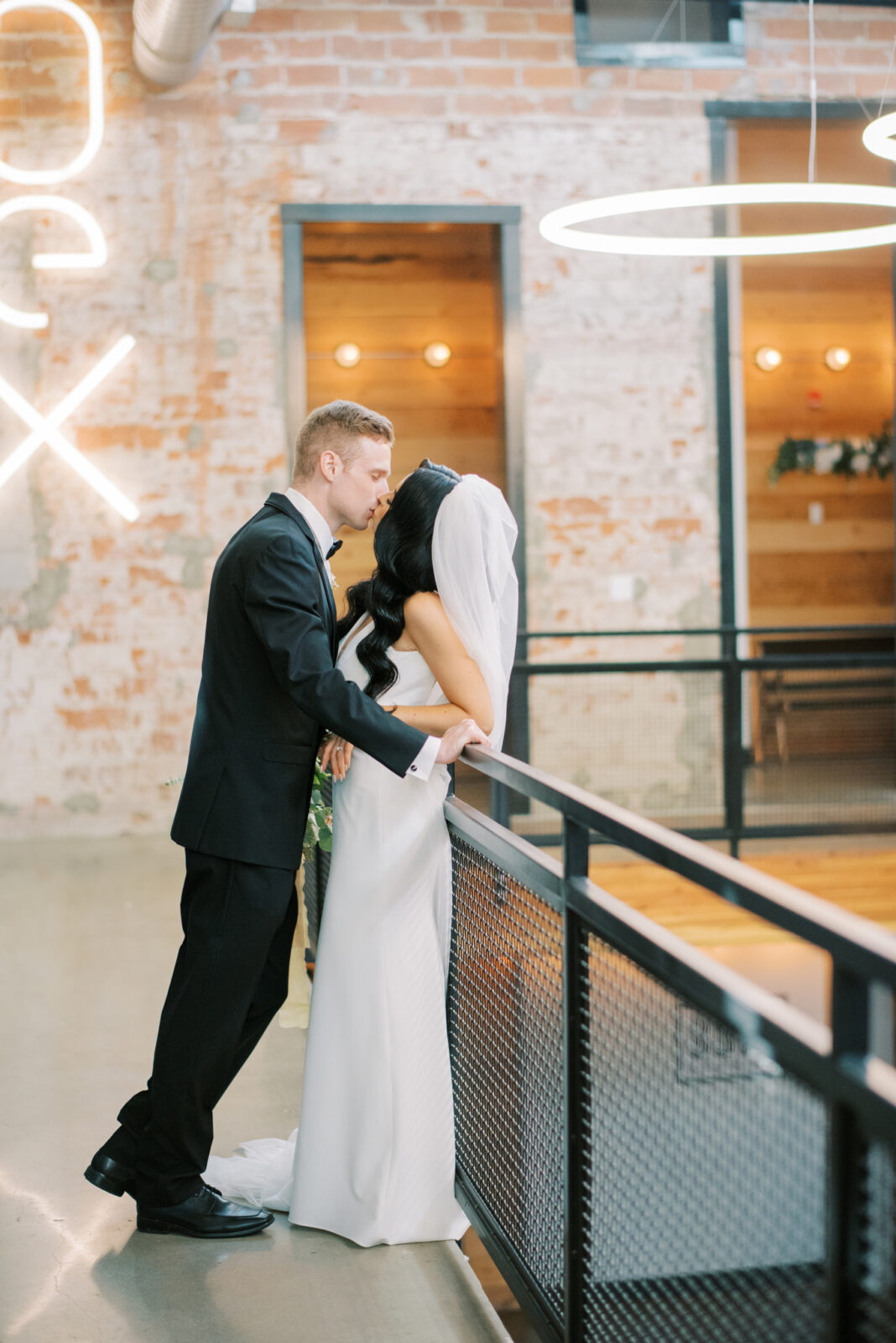 romantic bride and groom portraits on balcony with black industrial elements, wedding venue featuring trendy neon signs mounted on a brick wall