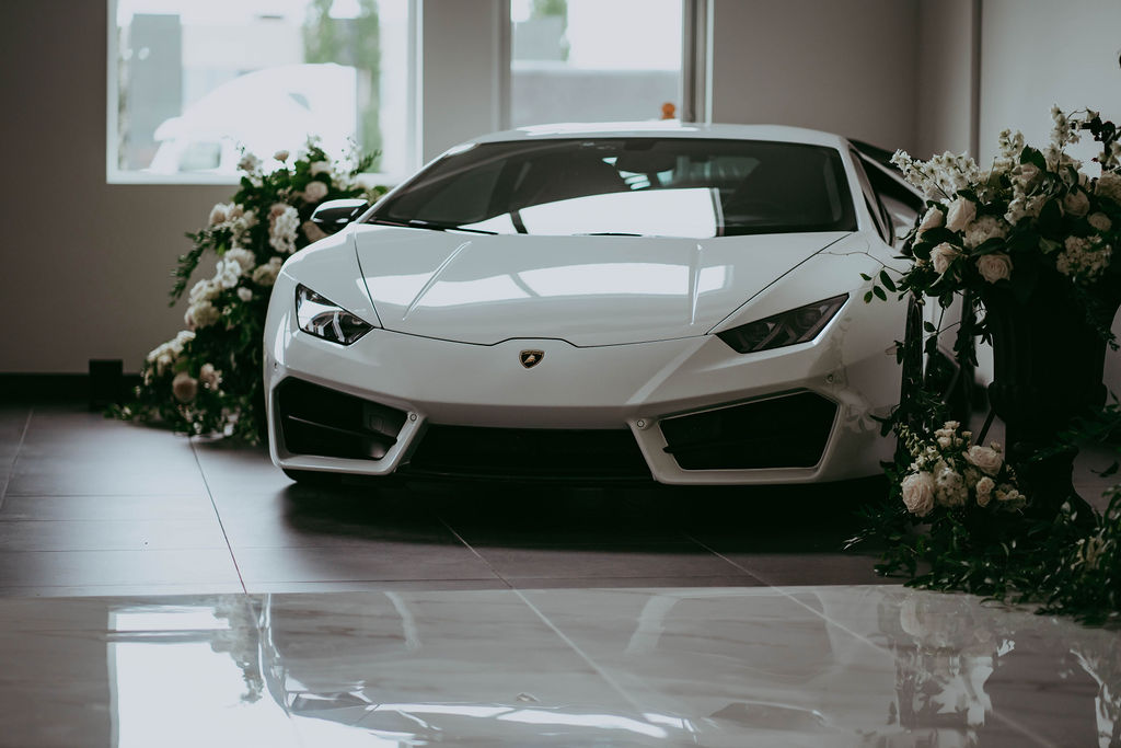 Luxury, exotic car in unique Red Deer wedding venue, surrounded by white floral arrangements and greenery. 