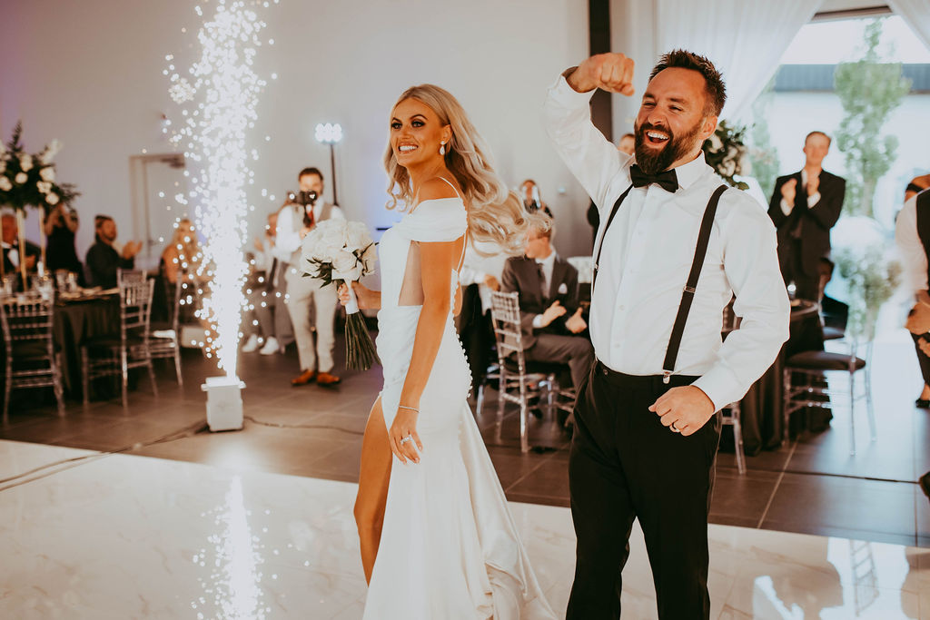 Bride and groom celebrating with their guests, surrounded by sparklers and guests applause at Red Deer wedding. Bride wearing modern wedding gown with slit, black and white wedding inspiration. 