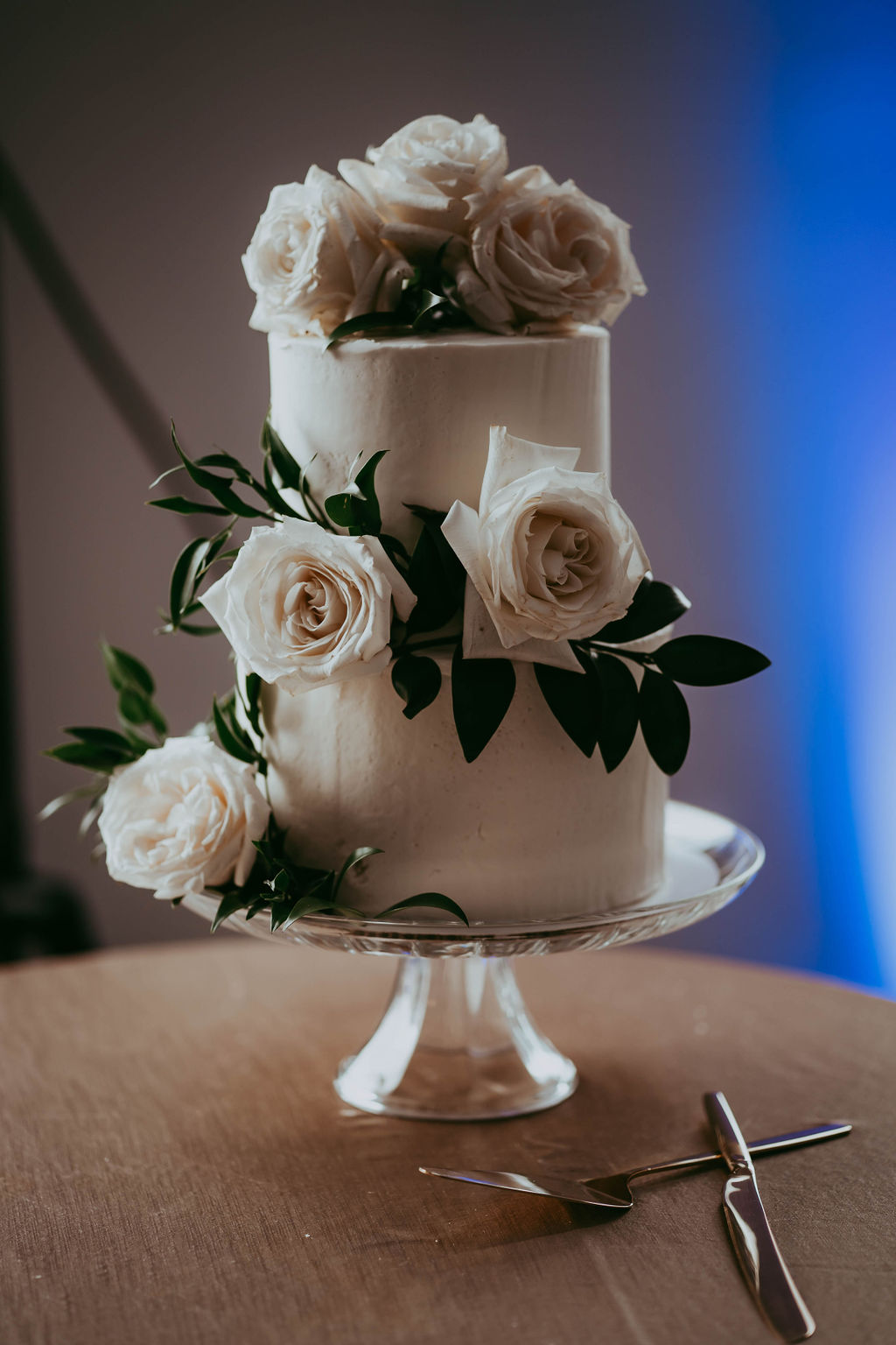 An elegant two-tiered wedding cake with white florals and added greenery at Red Deer wedding. 
