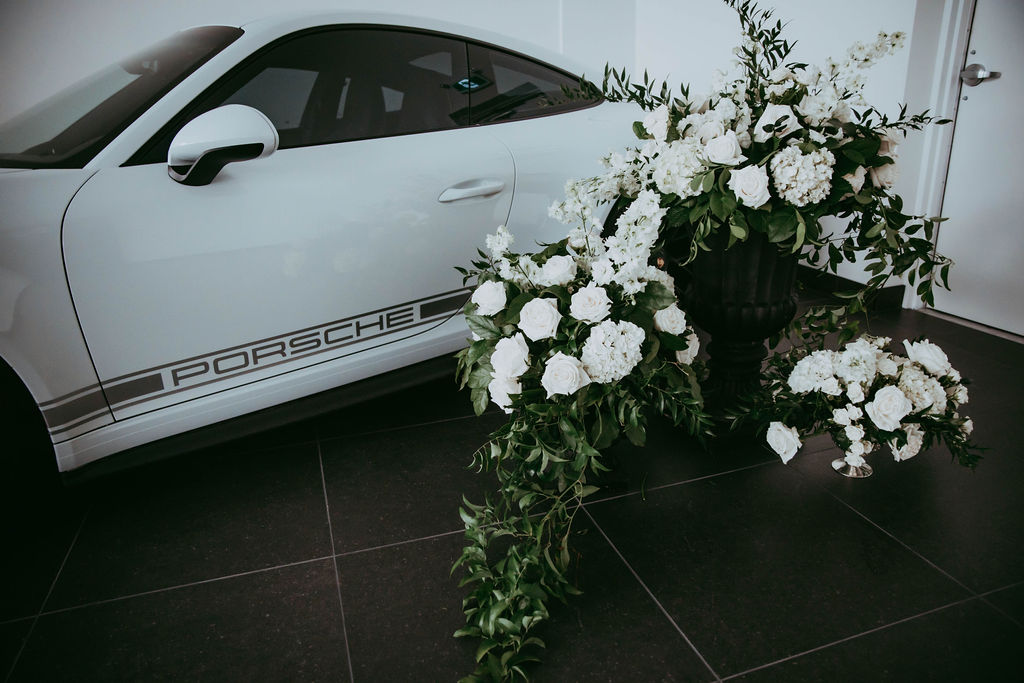 Black and white luxury car in Red Deer wedding venue, surrounded by white florals and added greenery. 