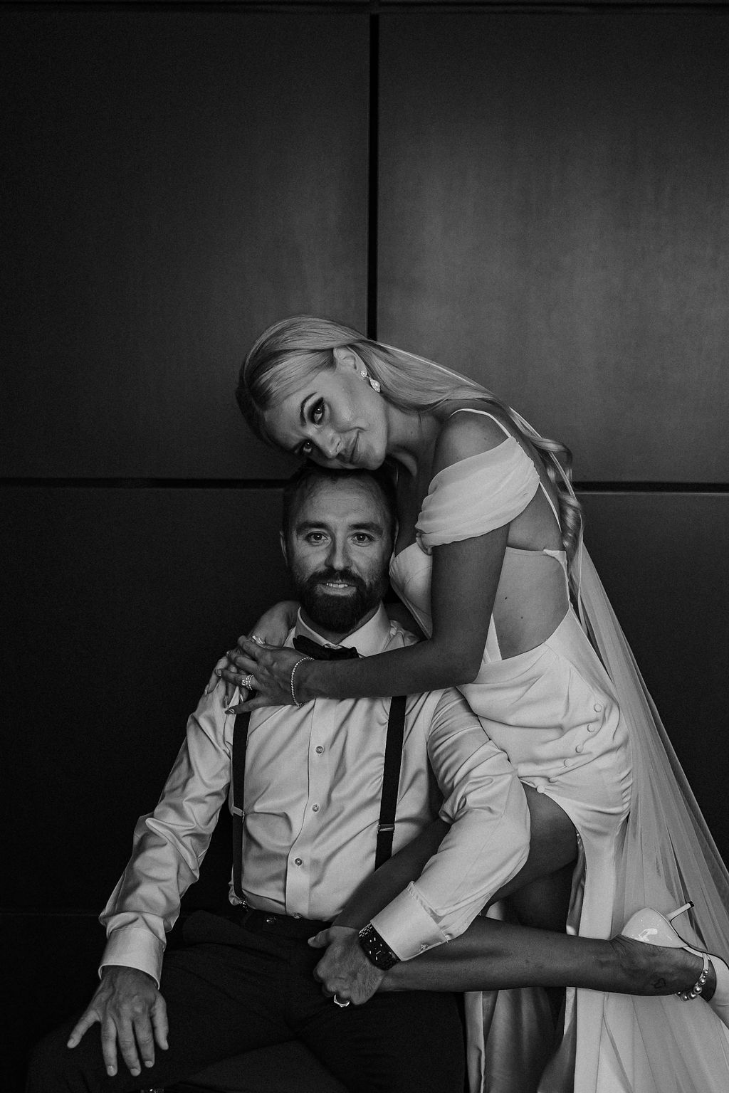 Glam wedding portrait inspiration with bride leaning on groom, wearing modern wedding gown with slit. 